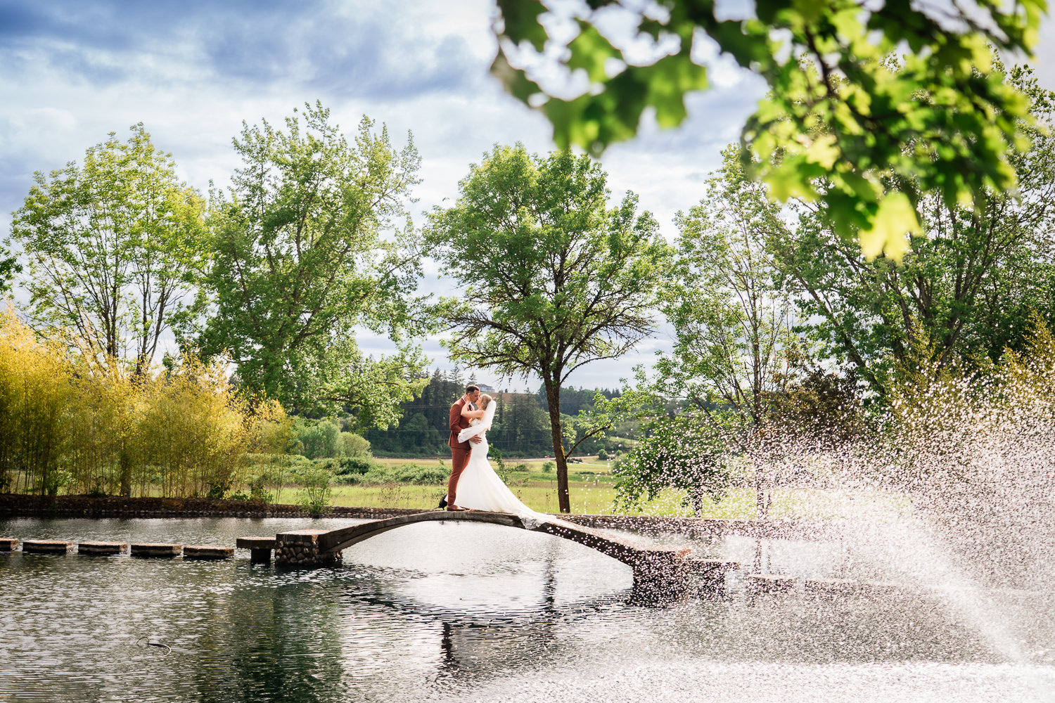 Water Oasis Wedding Portrait of bride and groom on the bridge with the water fountain in front of trees.